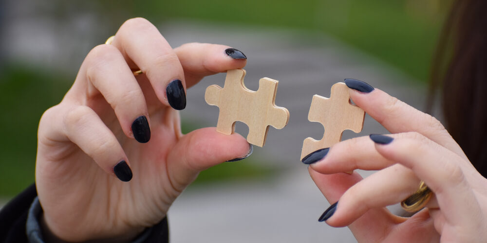 Person holding one jigsaw puzzle piece on each hand, bringing them closer to put them together